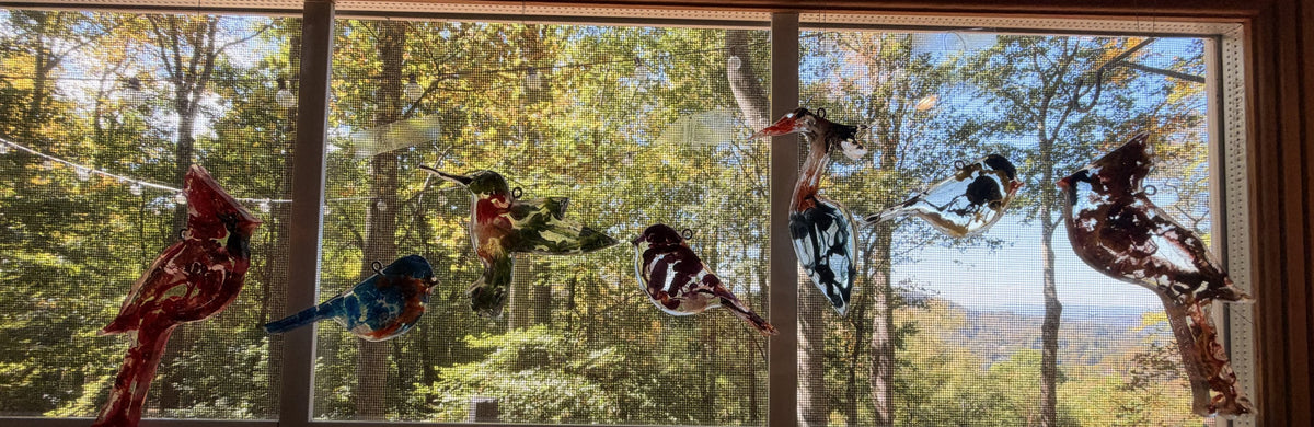 Resin bird ornaments hanging in a window with the Blue Ridge mountains behind