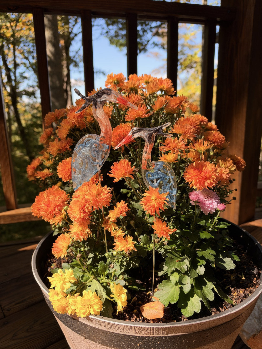 Two resin blue herons on sticks in orange mums