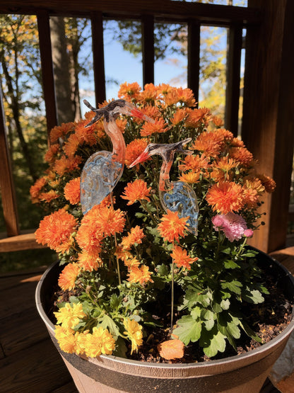 Two resin blue herons on sticks in orange mums