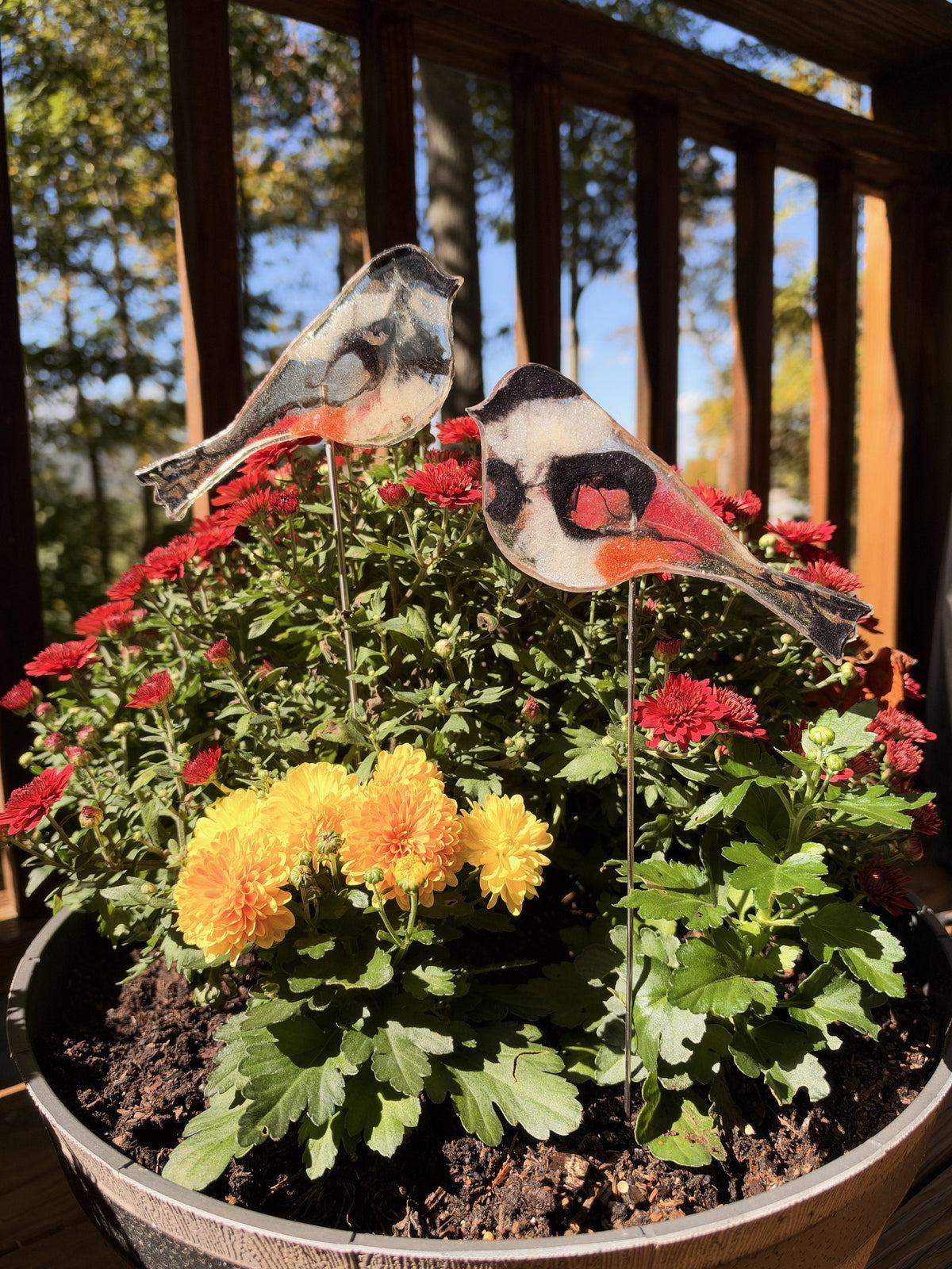 Two resin chickadees on sticks in red mums