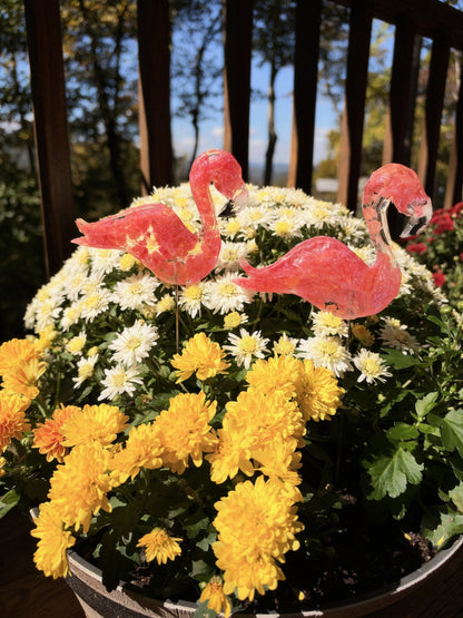 Two resin flamingos on sticks in white and yellow mums