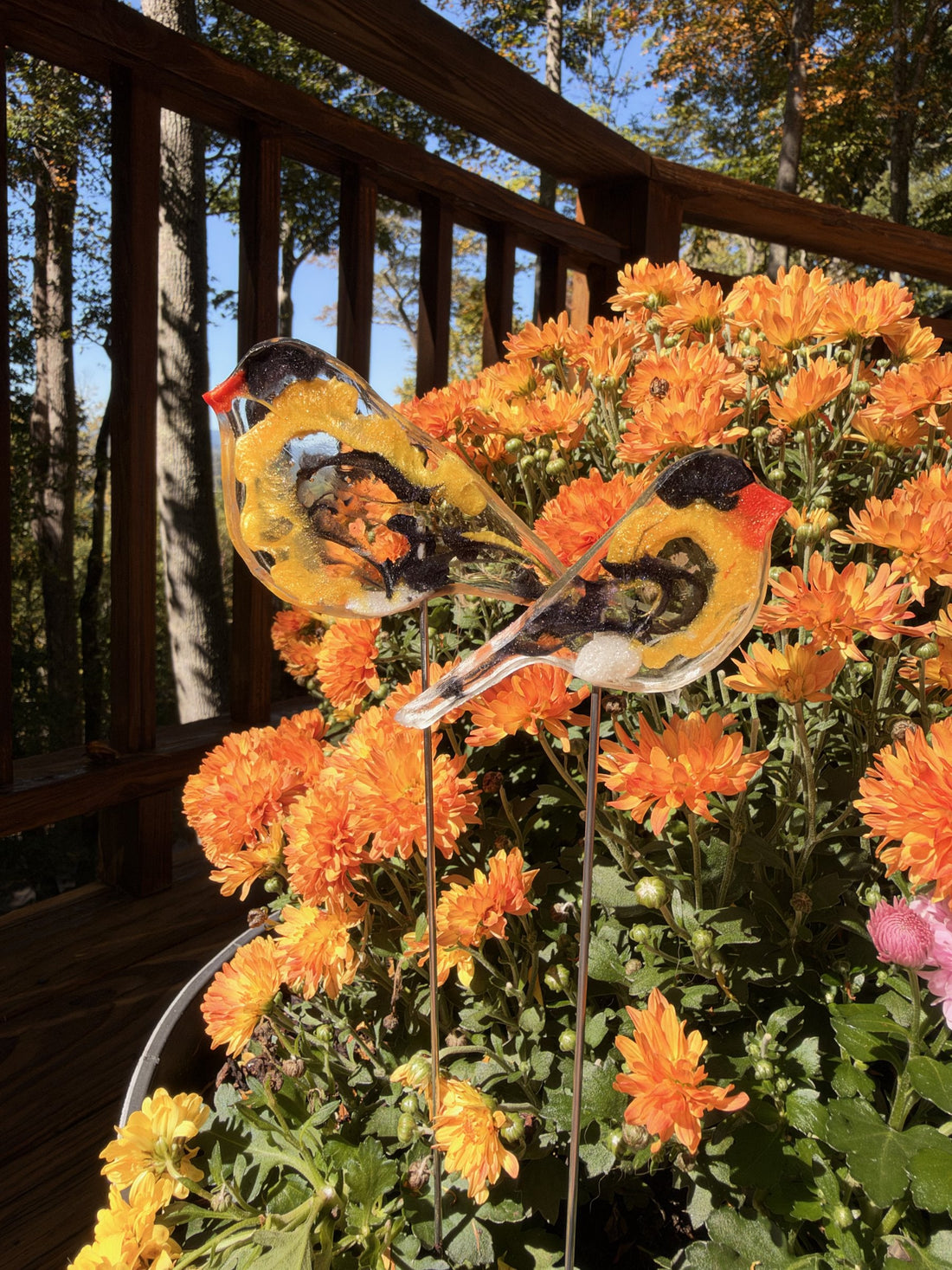 Two resin goldfinches on sticks in orange mums